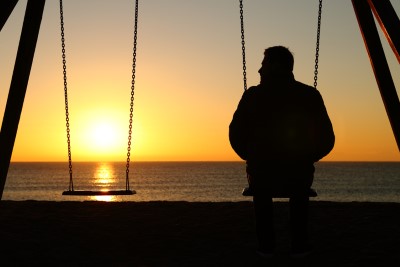 Man alone on a swing looking at empty seat
